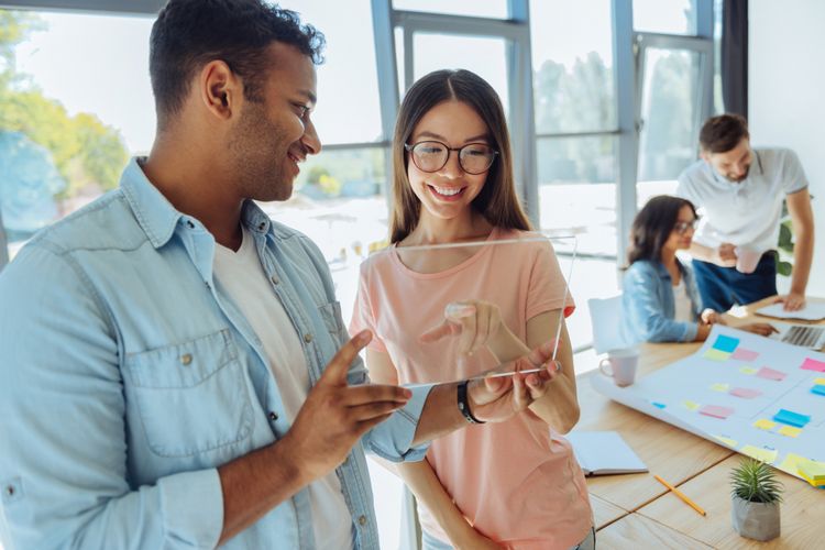 Try it. Delighted positive handsome man holding a tablet and showing it to his colleague while standing with her in the office