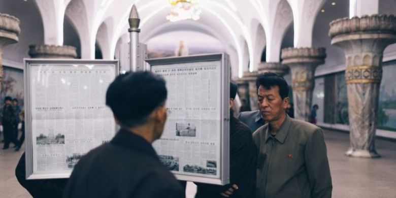 Beberapa orang terlihat sedang membaca papan surat kabar di stasiun kereta Pyongyang Metro, Korea Utara. 