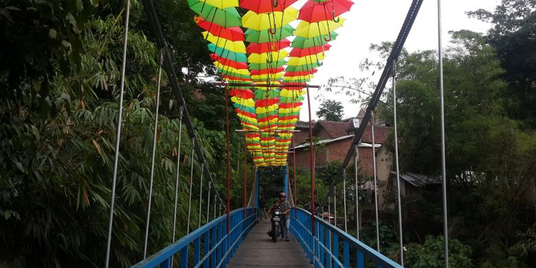 Seorang pengendara saat melintas di atas jembatan gantung di RT 6 RW 5 Kelurahan Penanggungan, Kecamatan Klojen, Kota Malang, Jawa Timur, Selasa (14/11/2017). Jembatan itu dihias dengan payung supaya kelihatan lebih indah.(KOMPAS.com/ANDI HARTIK)