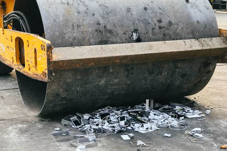 Mesin penggiling sesaat sebelum meggilas smartphone dan aksesori Oppo yang diletakkan di lantai beton di area terbuka.